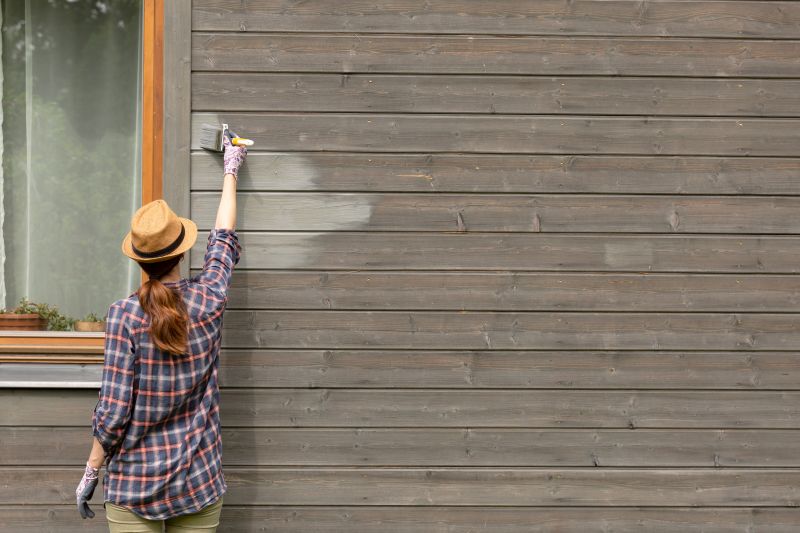 Woman worker painting wooden house exterior wall with paintbrush and wood protective color