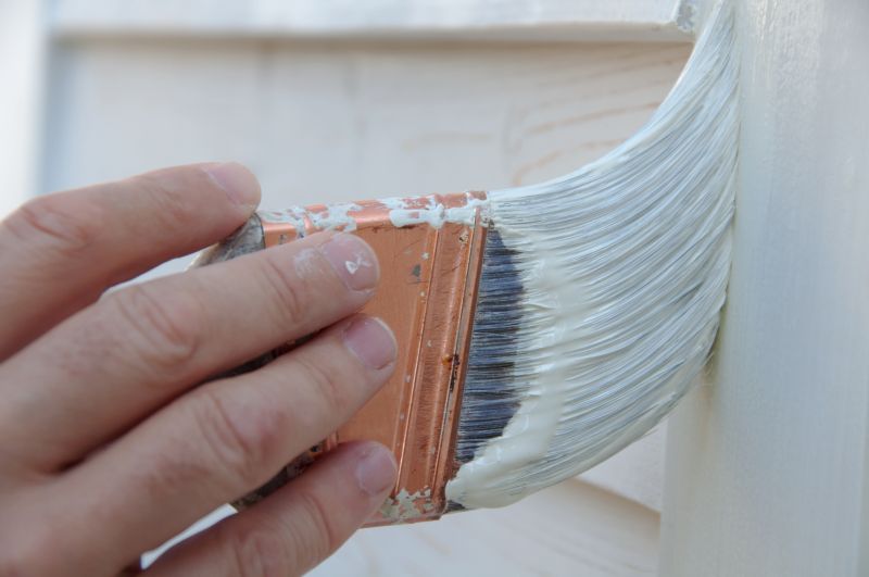 hand holding paint brush priming perpaired surface for exterior paint